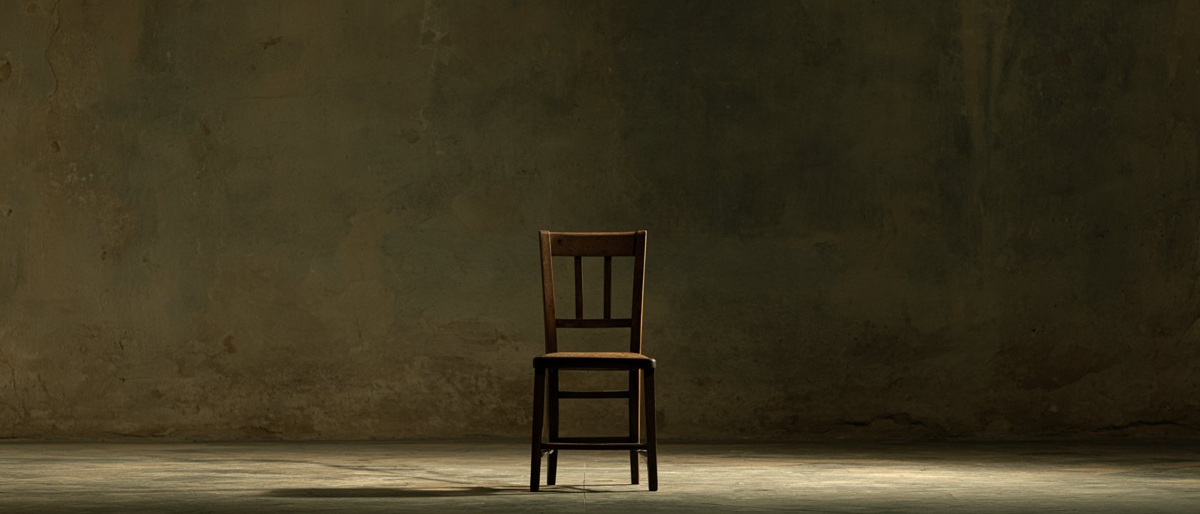 A single wooden chair facing camera in a bare plaster room, one soft light