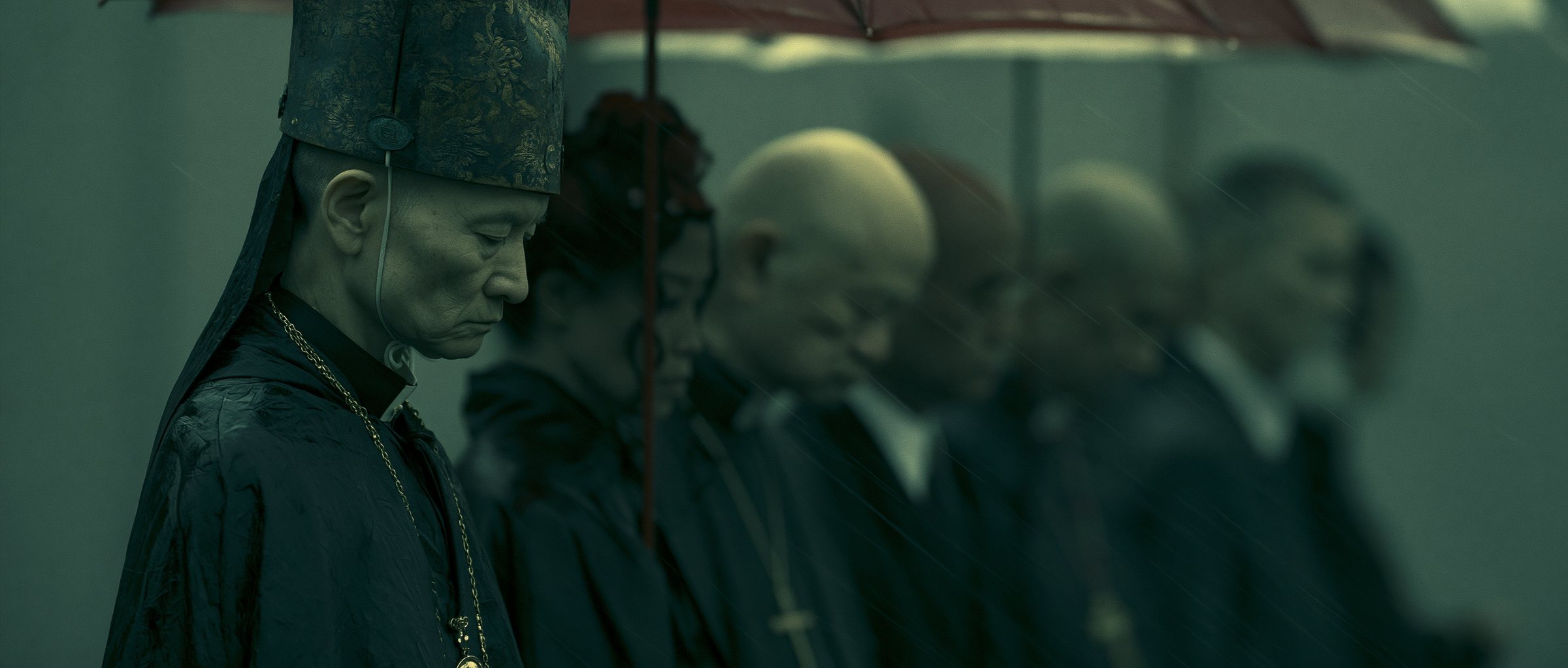 Bowed heads in the rain beneath a red umbrella