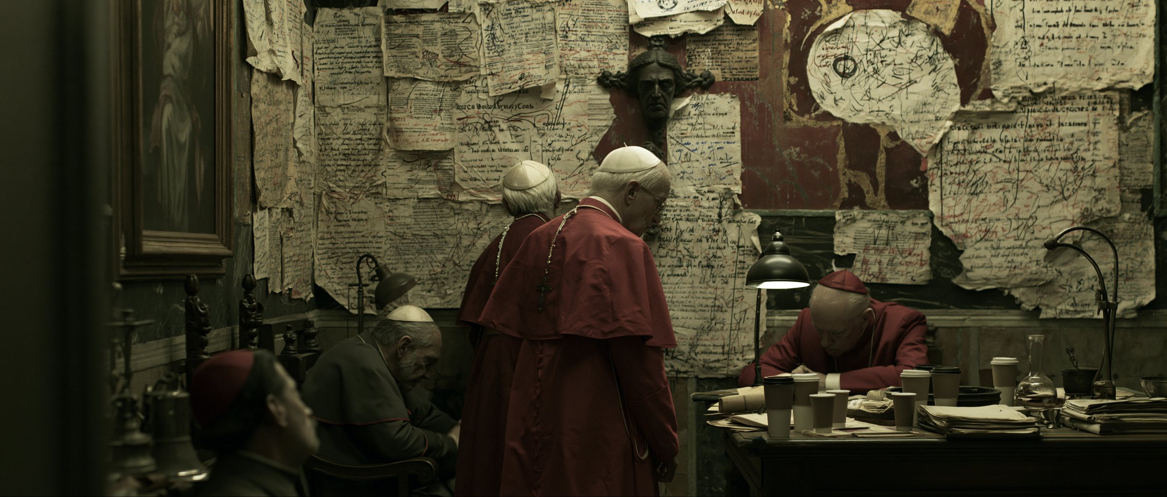 Cardinals working beneath a wall papered with annotated drafts