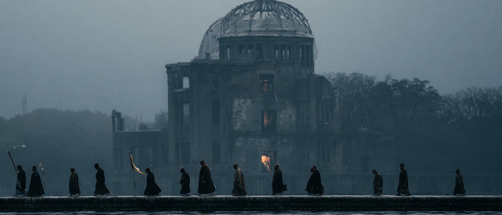A procession with a single torch passing before the Atomic Bomb Dome at dusk
